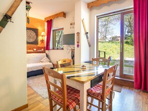 Ein gemütliches Zimmer mit einem Holztisch, Stühlen, einer Couch und einem großen Fenster mit Vorhängen.