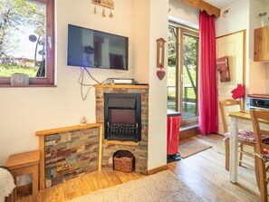 Ein gemütliches Zimmer mit Kamin, Fernseher, Essbereich und Blick auf die grüne Umgebung.