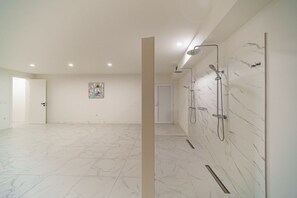 Ein geräumiges Badezimmer mit einer großzügigen Dusche, Marmorböden und einer Tür zu einem weiteren Raum.
