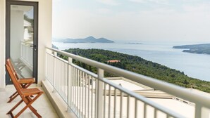 En balkon med to træstole og udsigt over et kystlandskab med bjerge og hav.