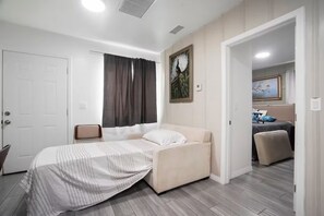 A bedroom with a bed, a chair, a door, and a painting on the wall.