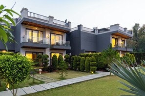 A modern two-story house with a well-maintained garden, large windows, and a balcony. - ELIVAAS Aranya Library Villas With Pool (Fatehpur Range)
