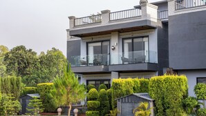 A modern two-story building with a balcony, a garage, and well-maintained landscaping. - ELIVAAS Aranya Library Villas With Pool (Fatehpur Range)