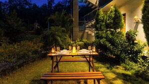 A dining table set outdoors with candles, surrounded by greenery and a staircase. - ELIVAAS Aranya Library Villas With Pool (Fatehpur Range)