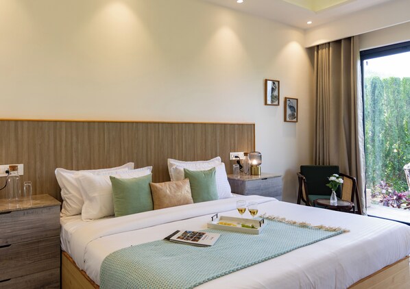 Una habitación de hotel con una cama grande, mesitas de noche, una silla y vistas a zonas verdes por la ventana.