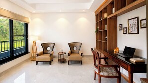A room with two armchairs, a desk with a laptop, a bookshelf, and a large window with a view of greenery. - ELIVAAS Aranya Library Villas With Pool (Fatehpur Range)
