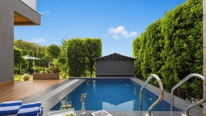 A swimming pool with a wooden deck, a glass of wine, and towels. - ELIVAAS Aranya Library Villas With Pool (Fatehpur Range)