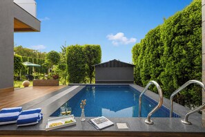Una piscina con cubierta de madera, una copa de vino y toallas.