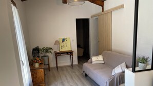 Une pièce comprenant un canapé, une petite table avec une lampe, une plante en pot et un tableau accroché au mur.