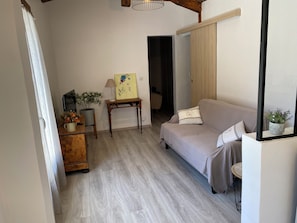 Ein Zimmer mit einer Couch, einem kleinen Tisch mit Lampe, einem Blumentopf und einem Bild an der Wand.