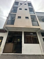 Un edificio de varios pisos con fachada de tejas, amplias ventanas y puerta de vidrio en la entrada principal.