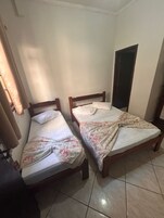 Dos camas individuales con cabeceros de madera, piso de baldosas y una ventana con cortinas.