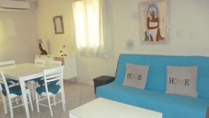 Ein Wohnzimmer mit einem blauen Sofa, zwei weißen Sesseln, einem weißen Tisch und einer kleinen weißen Kommode.