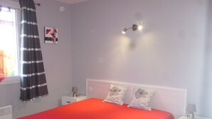 Ein Schlafzimmer mit Bett, Nachttischen, einer Lampe, einem Fenster mit Vorhängen und einer Wandleuchte.