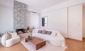 Ein modernes Wohnzimmer mit einem weißen Sofa, einem Holztisch und einem Kamin aus Stein.