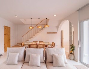 Ein modernes Interieur mit Essbereich, einer Couch, einer Treppe und großen Fenstern.