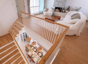 Un intérieur moderne avec un escalier en bois, un coin repas avec une table dressée pour quatre personnes et un salon avec un canapé et une cheminée.