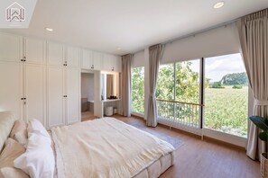 Un dormitorio con una cama grande, un escritorio y un armario. Tiene un balcón con vistas a zonas verdes.