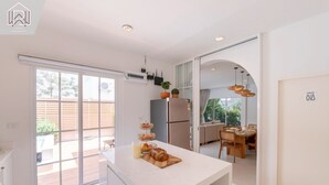 A modern kitchen with a large island, sliding glass doors to a patio, and a dining area visible through an archway. - Минималистичная вилла в Сарабури с видом на горы До 12 гостей (Tambon Song Khon)
