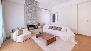 A modern living room with a white sofa, a wooden coffee table, and a stone fireplace. - Минималистичная вилла в Сарабури с видом на горы До 12 гостей (Tambon Song Khon)