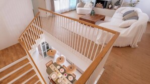 A modern interior with a wooden staircase, a dining area with a table set for four, and a white sofa in the background. - Минималистичная вилла в Сарабури с видом на горы До 12 гостей (Tambon Song Khon)