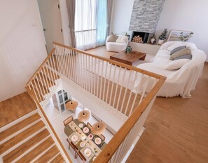 Un interior moderno con una escalera, una zona de comedor con una mesa dispuesta para cuatro personas y un sofá blanco al fondo.