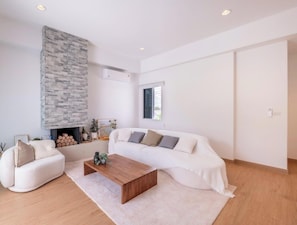 Een moderne woonkamer met een witte bank, een houten salontafel, een stenen openhaard en een groot raam.