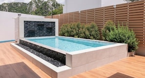 Una piscina rettangolare con un muro in pietra e una recinzione in legno sullo sfondo.
