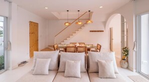 A modern interior with a dining area, sofa, staircase, and large windows.