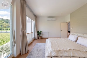 A bedroom with a large bed, a view of greenery outside, and a window with curtains. - Villa Kolam Minimalis Pemandangan Gunung di Saraburi 12 Pax (Tambon Song Khon)