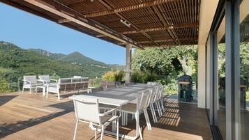 Een terras buiten met een houten pergola, een eettafel met stoelen en uitzicht op bergen.