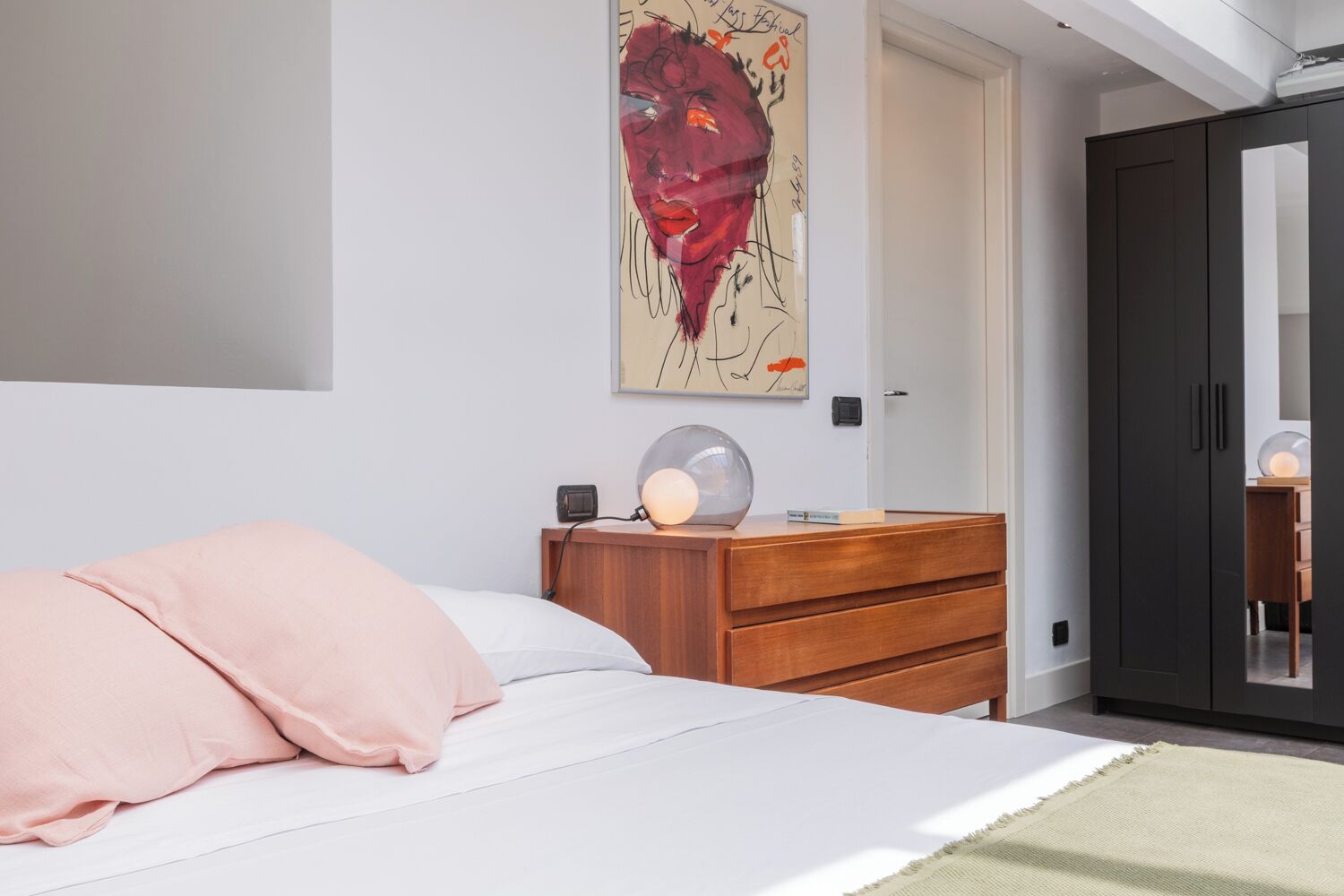 Une chambre à coucher comprenant un lit, une commode, une table de chevet, une lampe, un tableau et une armoire.