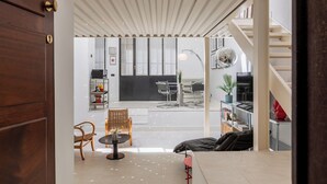 Un espacio abierto que incluye zona de estar con mesa de comedor, sillas, sofá y una escalera que sube a un nivel superior.