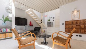 Una sala de estar moderna con dos sillones de mimbre, una mesa redonda, un televisor y una escalera.