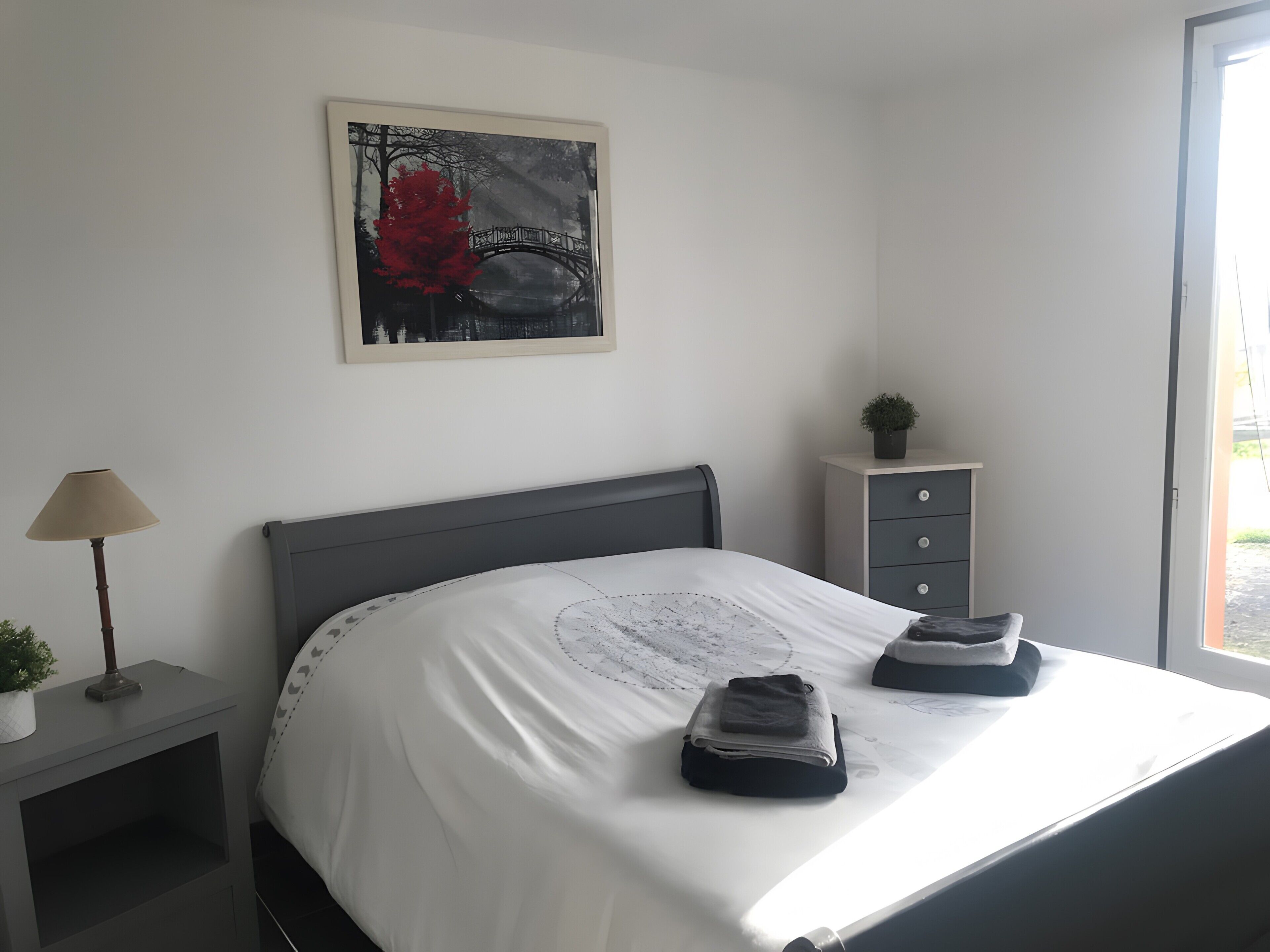 A bedroom with a bed, a nightstand with a lamp, a dresser, and a framed picture on the wall.