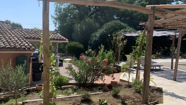 A garden with a pergola, a patio area, and a small table with chairs.