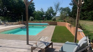 A wooden deck with a pool, lounge chairs, and a small table.