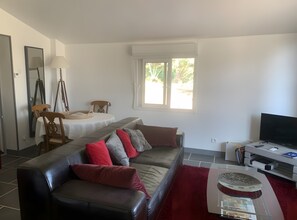 Un salon avec un canapé, un téléviseur, une table avec une lampe et une fenêtre.