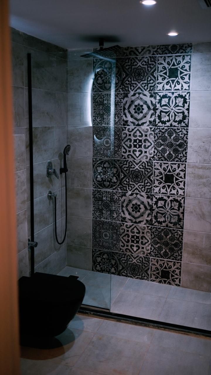 A shower with a glass door and a tiled wall with intricate patterns.