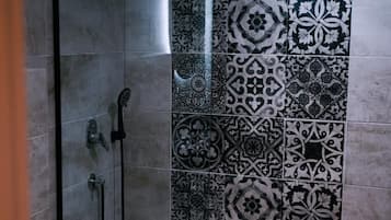 A shower with a glass door and a tiled wall with intricate patterns.