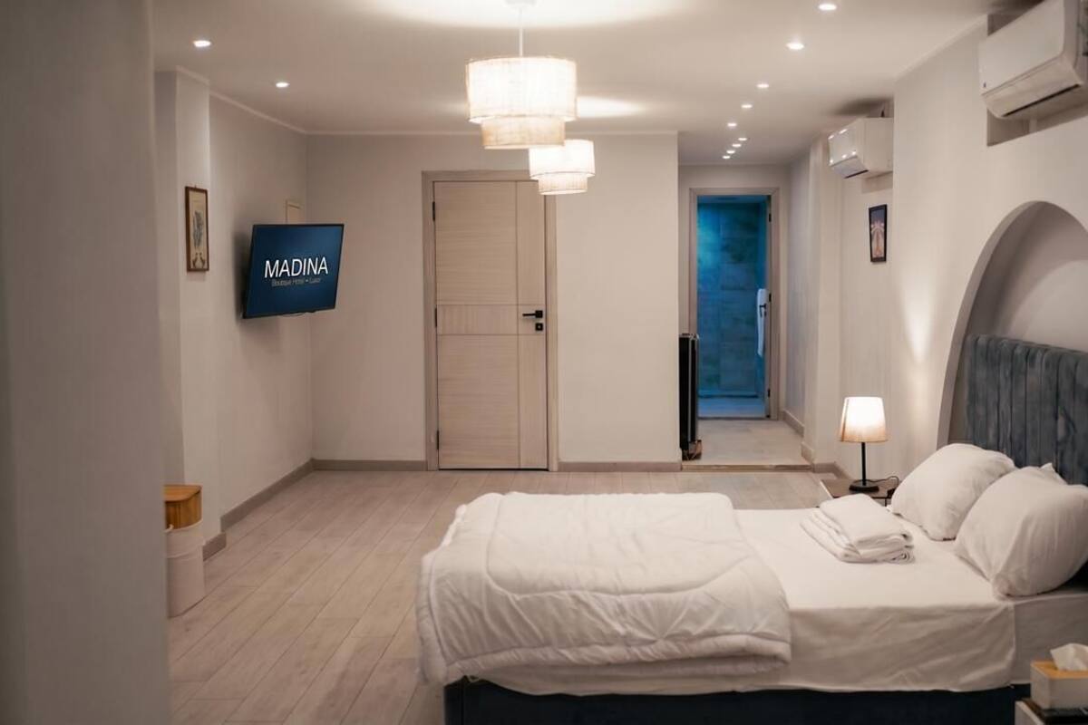 Ein Hotelzimmer mit Bett, Fernseher, Tür und einem Flur, der auf einen Balkon führt.