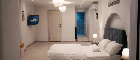 A hotel room with a bed, a TV, a door, and a hallway leading to a balcony.