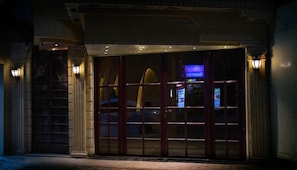 A building entrance with a large glass door, a stone facade, and two wall-mounted lights.