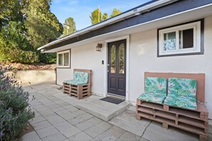 Ein kleines Haus mit einer Haustür, zwei Fenstern, einer Veranda mit hölzernen Bänken und einem Garten.