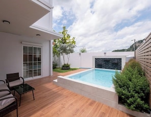 Un espace piscine extérieur moderne, doté d’une terrasse en bois, d’une entrée avec porte vitrée et d’un petit coin salon.