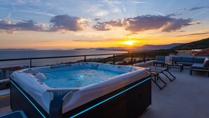 Eine Dachterrasse mit Whirlpool, Sitzgelegenheiten im Freien und Blick auf den Sonnenuntergang über dem Meer.