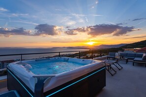 A rooftop terrace with a hot tub, outdoor seating, and a view of the sunset over the sea.