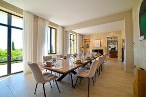 A spacious dining area with a long table set for a meal, large windows, and a view of greenery outside. - Le Domaine de Laudun · 8 bedrooms · private pool (Tarascon)