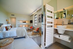 A modern bedroom with a bed, bedside tables, a chair, a sofa, and a bathroom with a sink and mirror. - Le Domaine de Laudun · 8 bedrooms · private pool (Tarascon)