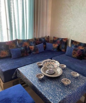 Ein Zimmer mit einer Sofagarnitur, einem Tisch mit Dekoration und einem Fenster mit Vorhängen.